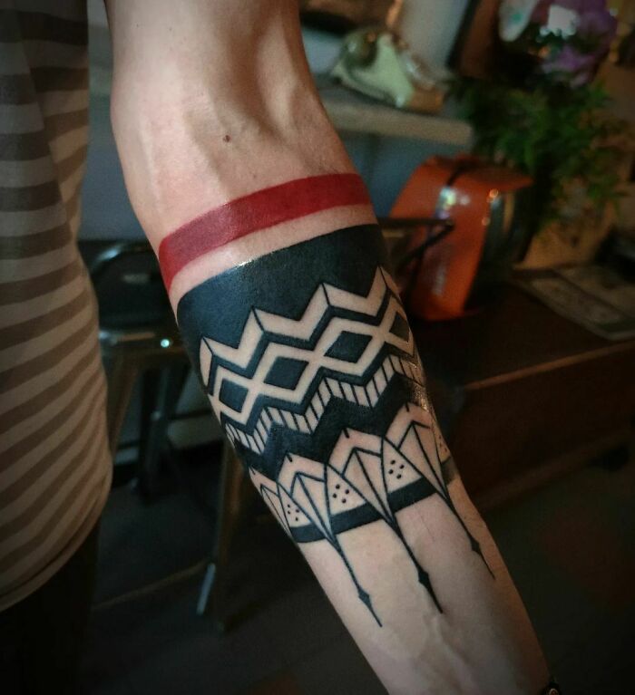 Geometric armband tattoo design in black and red featuring intricate patterns on a person's forearm.