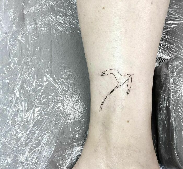 Fine-line tattoo of a single-line bird on forearm against a textured background.