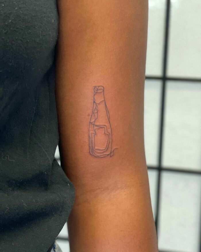 Minimalist line tattoo of a wine bottle on an arm, showcasing unique line tattoo art.