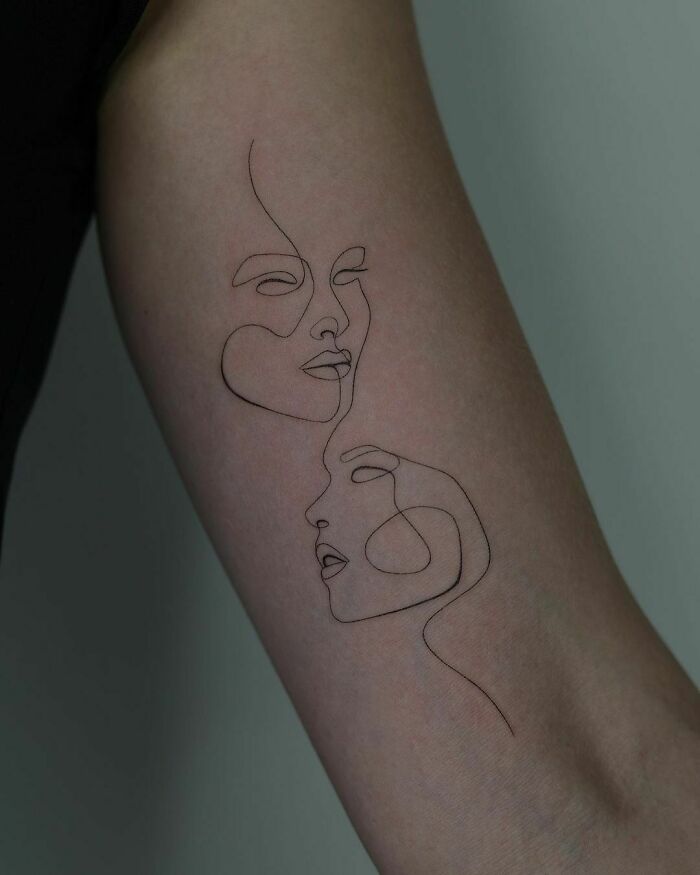 Minimalist line tattoo on an arm with two abstract faces.
