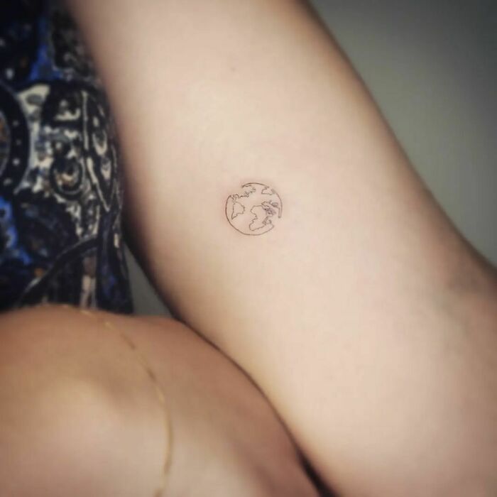 Minimalist single-line tattoo of a globe on an arm, showcasing earthy art.