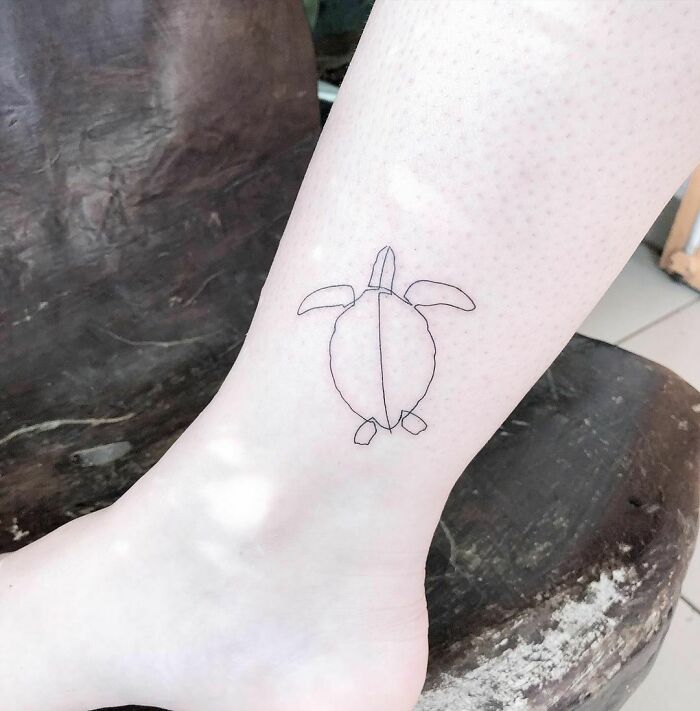Single-line tattoo of a turtle on a person's leg, showcasing minimalist design.
