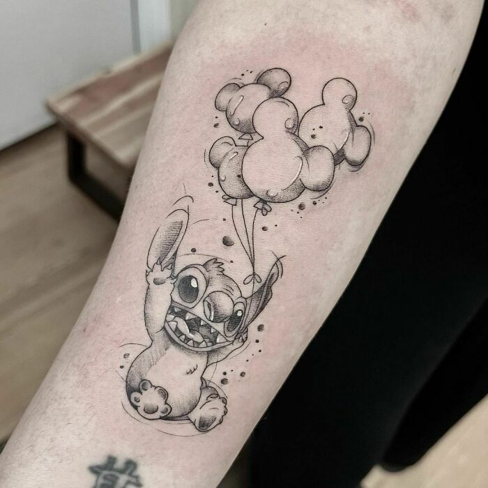 Cartoon tattoo featuring a playful character Stitch with balloons on an arm, capturing a nostalgic vibe.