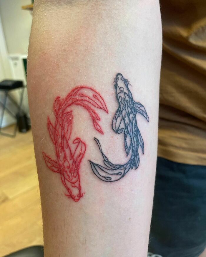 Fine-line tattoo of two koi fish in red and black ink on an arm.