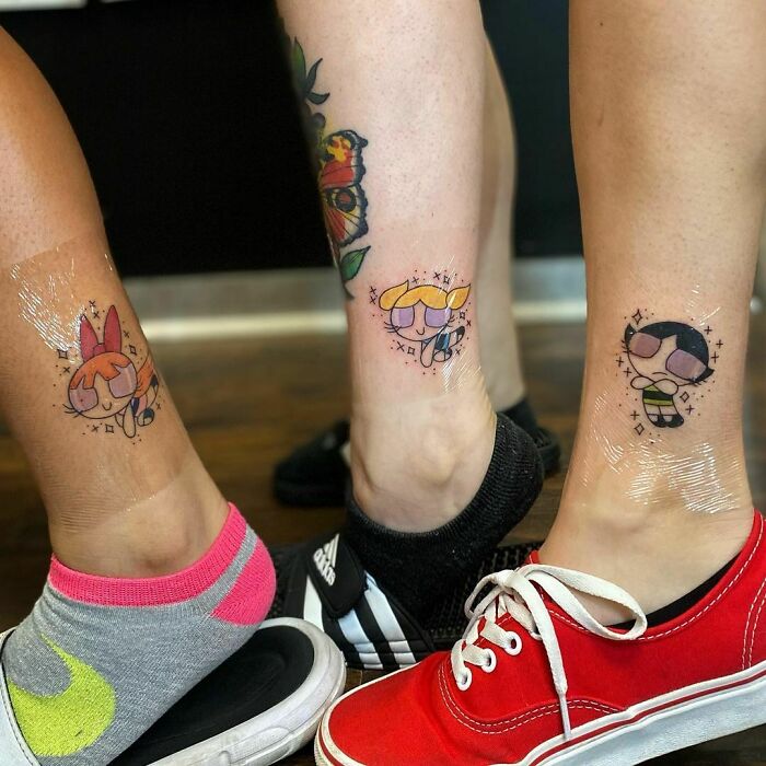 Three friends display matching tattoos on their legs, celebrating friendship with cartoon characters.