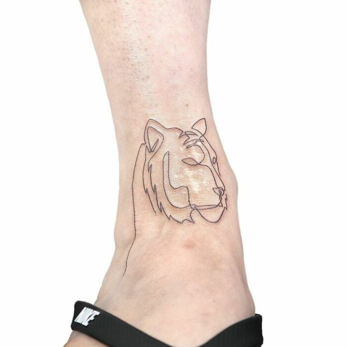 Single-line tattoo of a lion's head on an ankle, showcasing minimalist art.