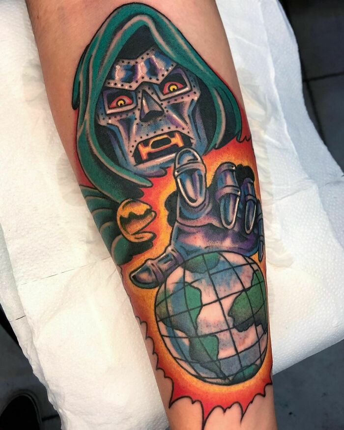 Colorful Marvel tattoo featuring a character in a hood and metal mask with a globe in fiery hand.