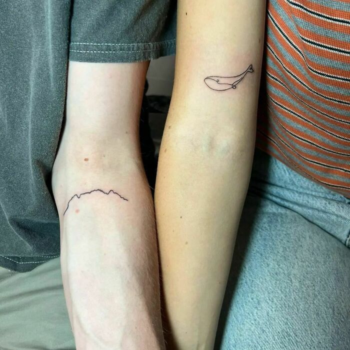 Fine-line tattoos on arms, featuring a whale and a mountain outline.