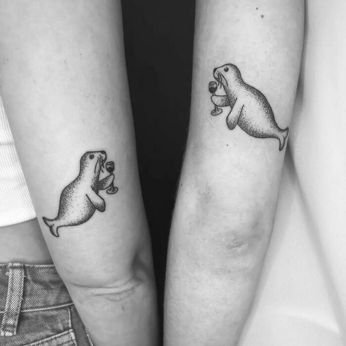 Seal-themed BFF tattoos on forearms, each holding a wine glass, symbolizing friendship and shared adventures.