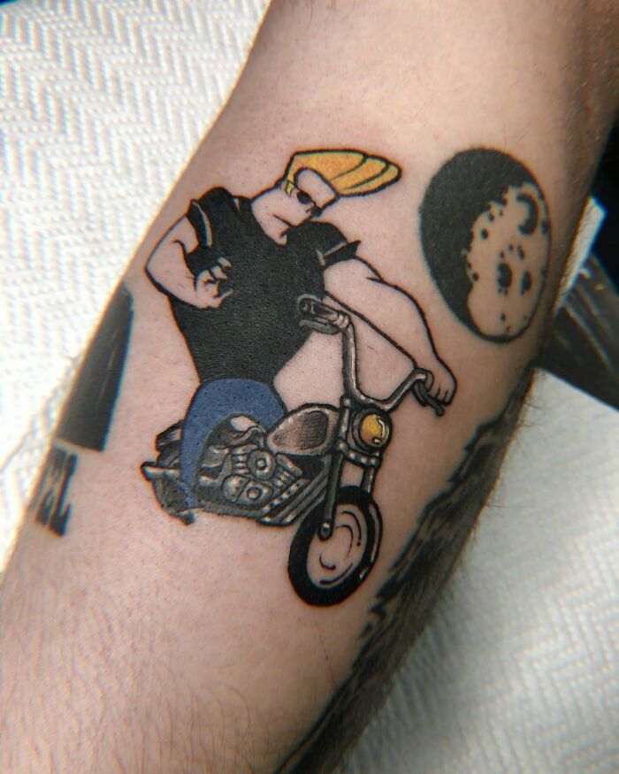 Cartoon tattoo of a character with blond hair on a motorcycle, evoking childhood favorites.