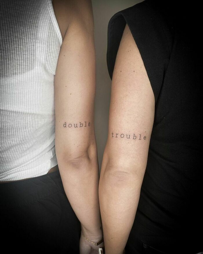 Best friend tattoos on arms with "double" and "trouble" text, symbolizing friendship.