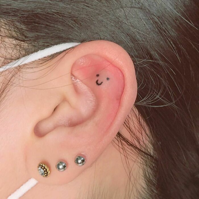 Minimal ear tattoo with a smiling face on the inner cartilage.