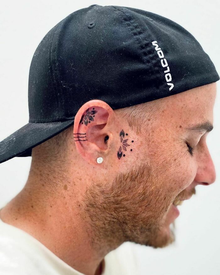 Man wearing a cap with unique ear tattoo design featuring lines and floral patterns.