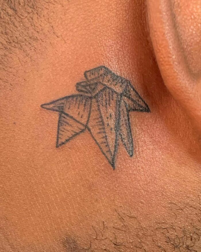 Origami-style ear tattoo on skin, featuring geometric shapes and fine line details.