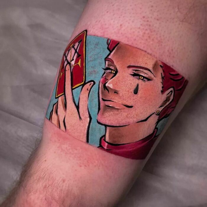 Cartoon tattoo on arm depicting a character with a smile, holding a card, and a teardrop under one eye.