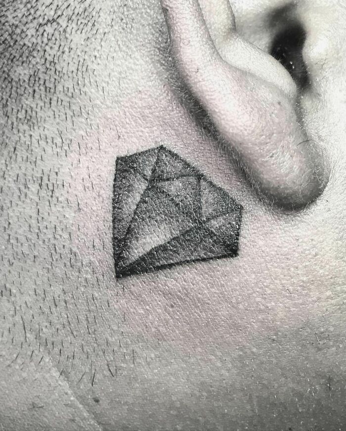 Ear tattoo of a geometric diamond design, combining subtle detail with bold style.
