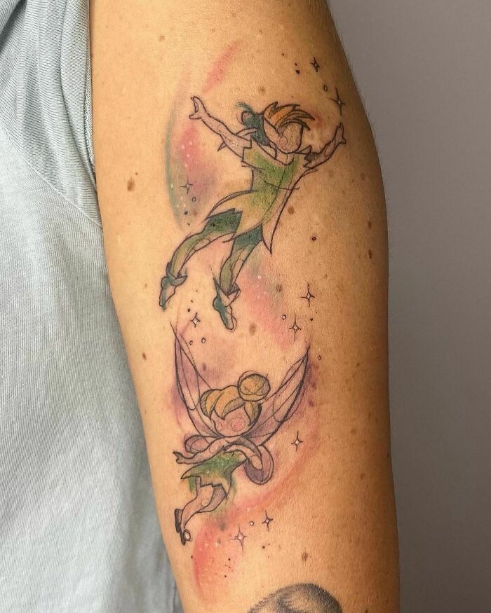 Cartoon tattoo of two flying characters from animated shows on an arm, with colorful background and stars.