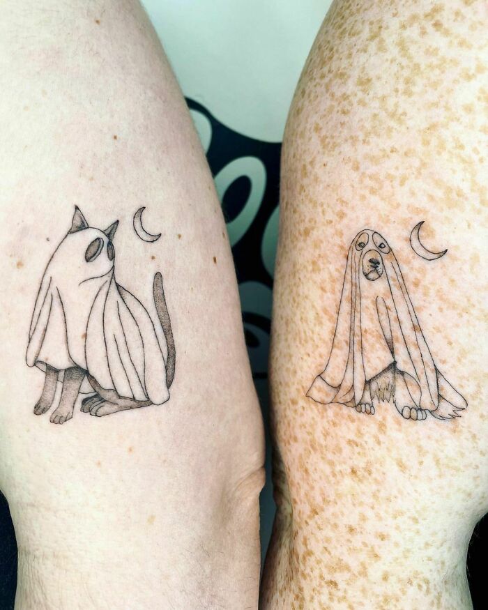 Matching best friend tattoos of a cat and dog in ghost costumes with crescent moons on arms.