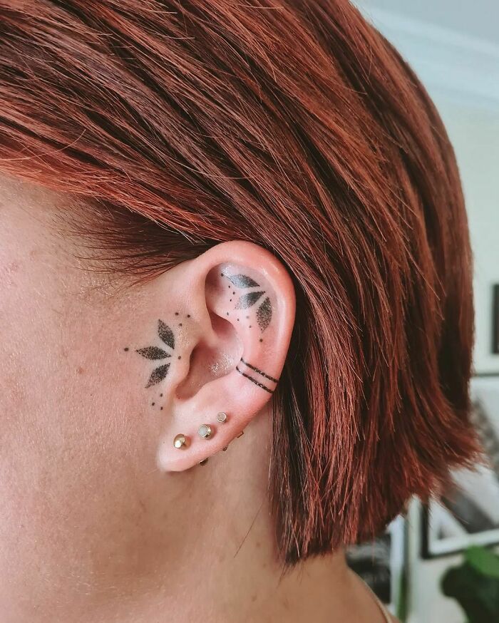 Stylish ear tattoo with geometric shapes and piercings, showcasing unique body art choices.