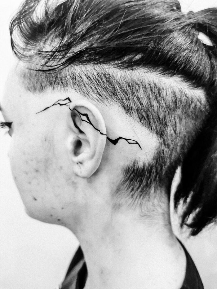 Ear tattoo idea featuring minimalist mountain design behind the ear on shaved side hairstyle.