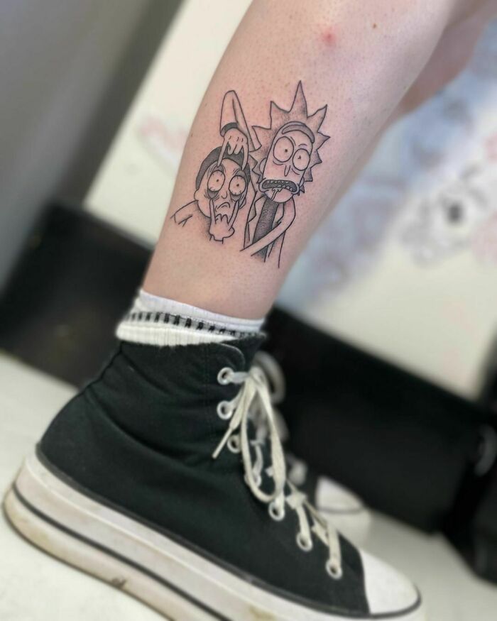 Cartoon tattoo of two characters on a person's leg, wearing black sneakers.