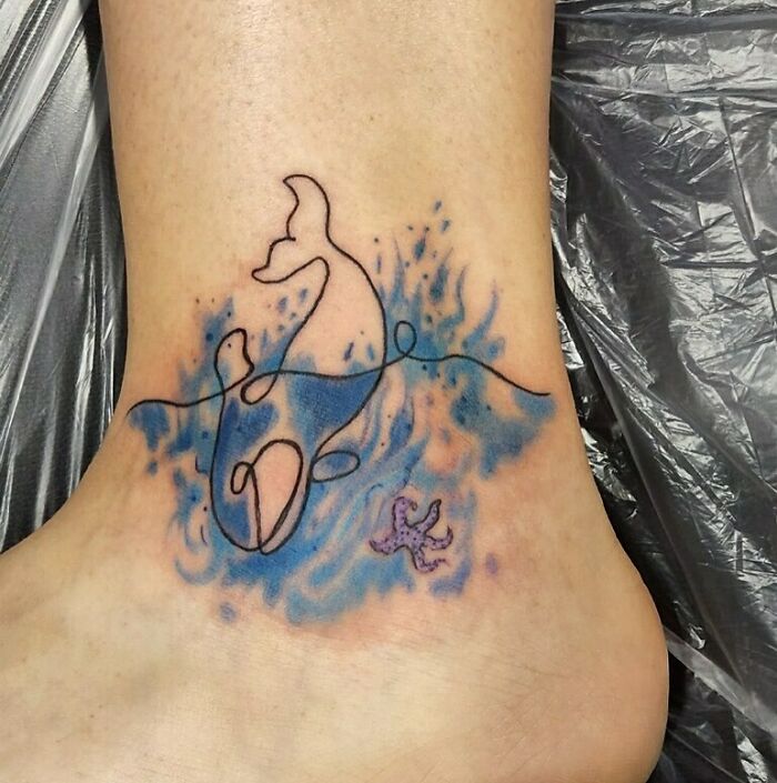 Linear tattoo of dolphins with blue waves on a person's foot, ideal for minimalism enthusiasts.