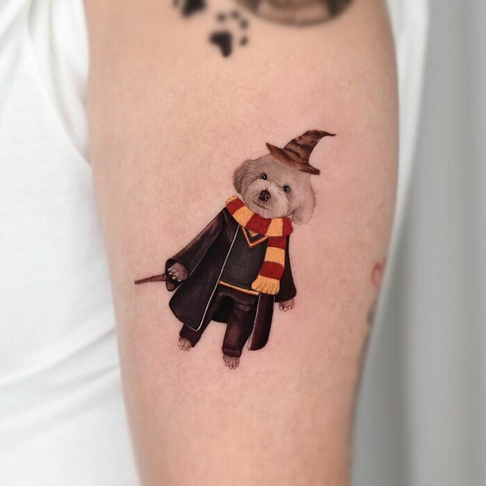 Cute dog in wizard outfit tattoo, wearing a Hogwarts scarf and hat, ideal for Harry Potter fans.