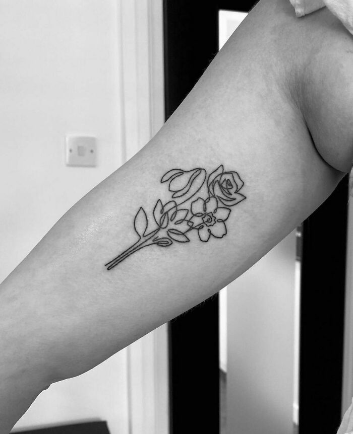 Single-line tattoo of flowers on a person's forearm, showcasing delicate and minimalist design.