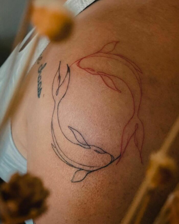 Single-line tattoo of two koi fish on an arm, designed in minimalist black and red ink.