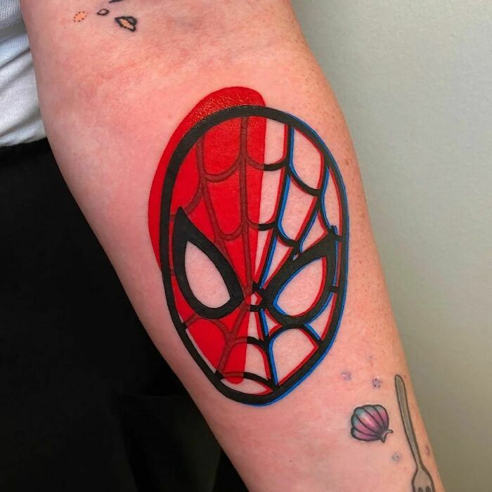 Marvel tattoo of a Spider-Man mask on forearm, vibrant red and blue colors with bold outlines.