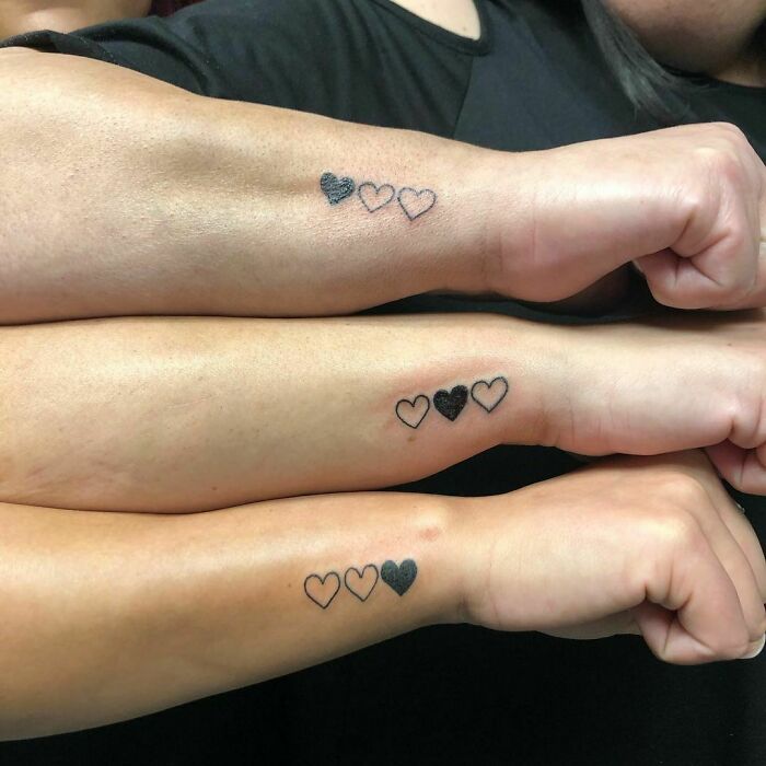 Three forearms with matching heart tattoos symbolizing friendship.