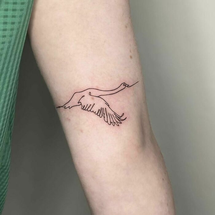 Single-line tattoo of a flying bird on forearm, showcasing minimalist art style.