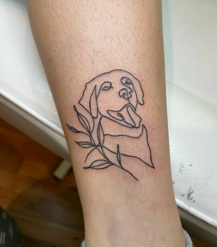 Minimalism tattoo with a line art dog and leaves on a person's leg.