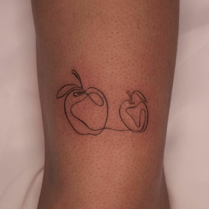 Single-line tattoo of two apples on skin, showcasing fine-line perfection.