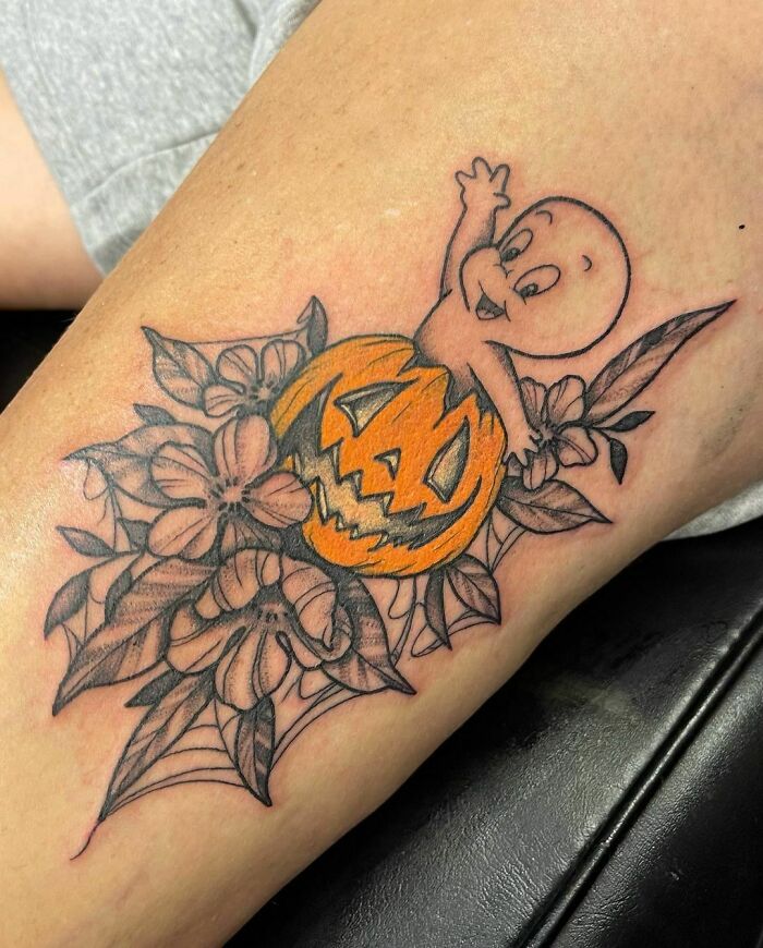Cartoon tattoo of a playful ghost emerging from a carved pumpkin among floral designs.