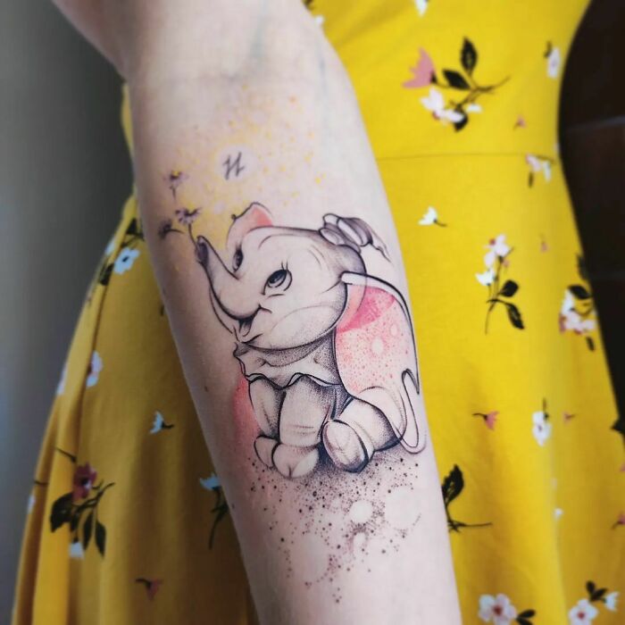 Dumbo cartoon tattoo on forearm with colorful background, showcasing nostalgic body art.