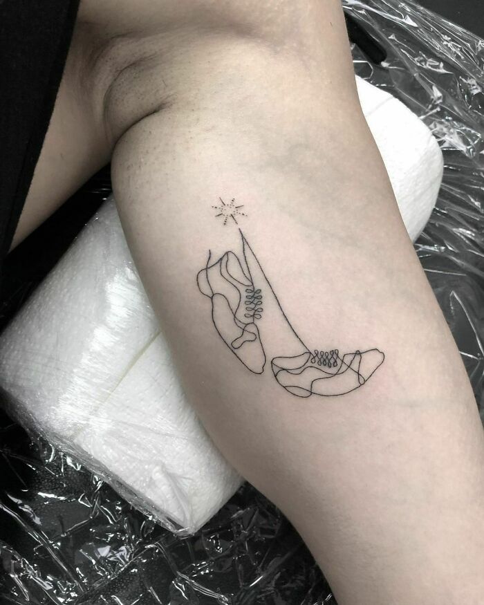 Single-line tattoo of sneakers and high heels on a person's arm with a small star design.
