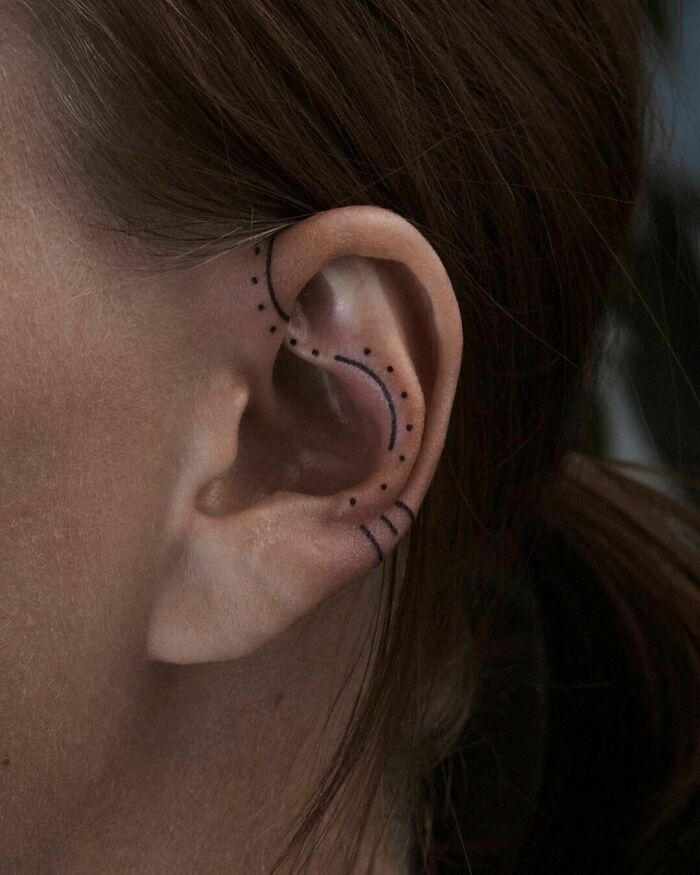 Minimalist ear tattoo with dotted lines along the ear's curve.
