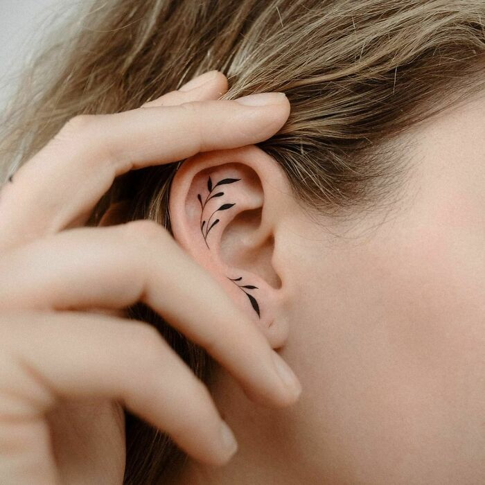 Minimalist leaf ear tattoo on woman's inner ear.
