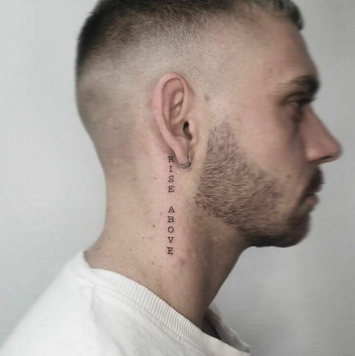 Side profile of a man with "Rise Above" tattoo behind the ear.