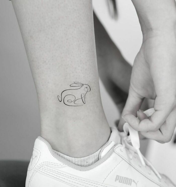 A single-line tattoo of a rabbit on an ankle, showcasing fine-line perfection.