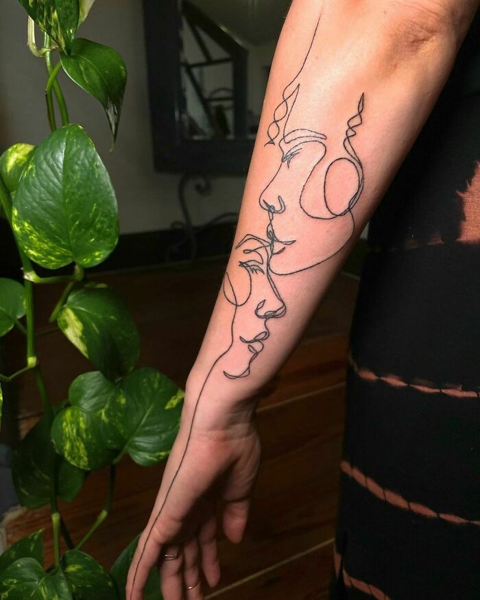 Minimalist line tattoo featuring intertwined faces on a person's forearm, beside a leafy plant.