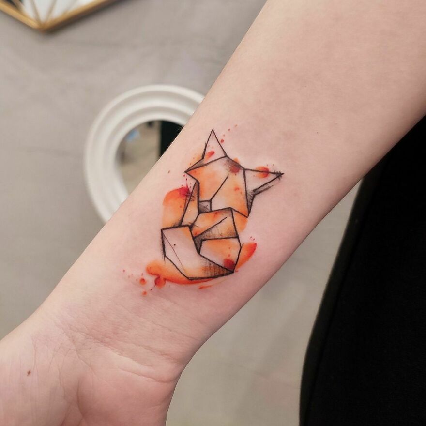 Geometric fox watercolor tattoo with orange accents on forearm.