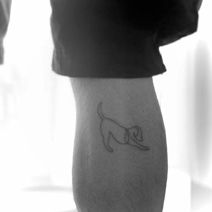 Minimalist line tattoo of a downward-facing dog on a person's leg.