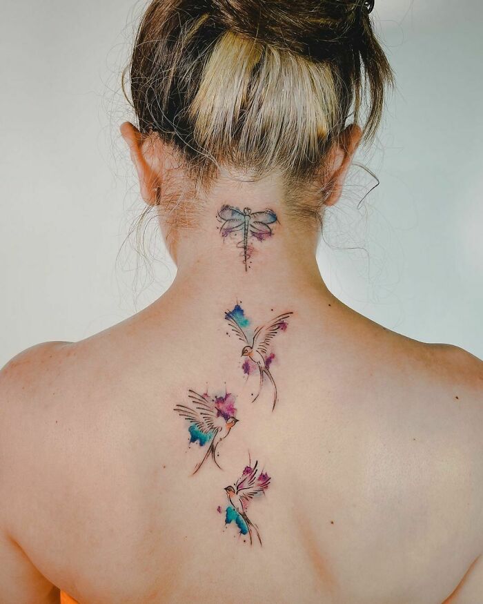 Watercolor tattoo with ethereal birds and a dragonfly on a woman's back.