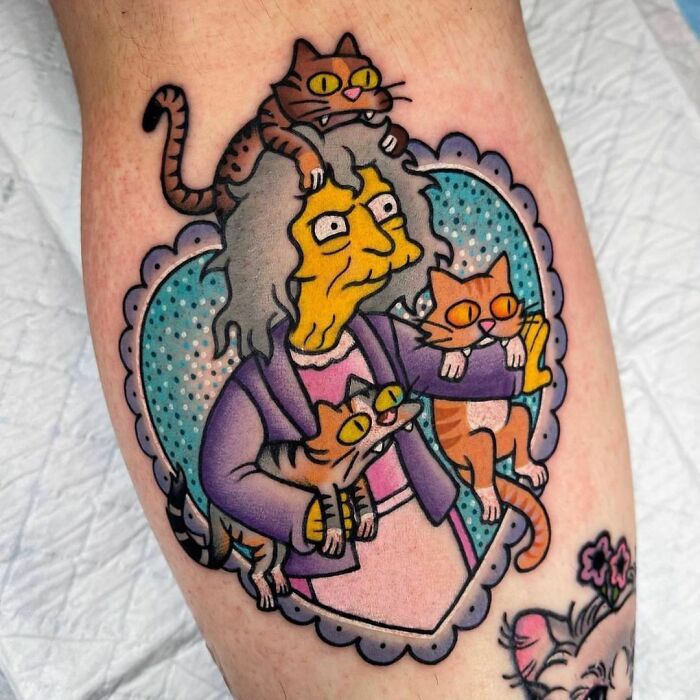 Cartoon tattoo of an elderly woman surrounded by four cats in a colorful, whimsical style.