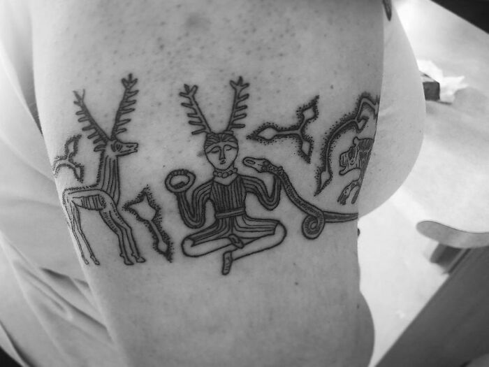 Close-up of an intricate tribal armband tattoo design featuring symbolic figures on an upper arm.