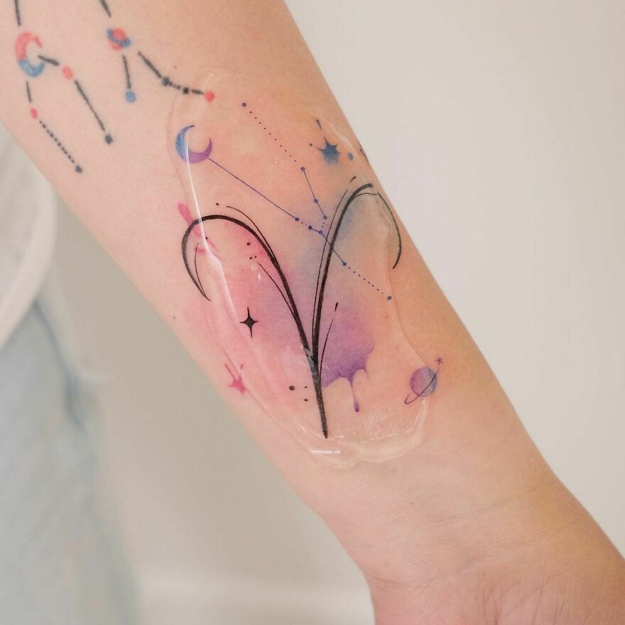Watercolor tattoo featuring an abstract constellation design with soft pastel shades on a forearm.