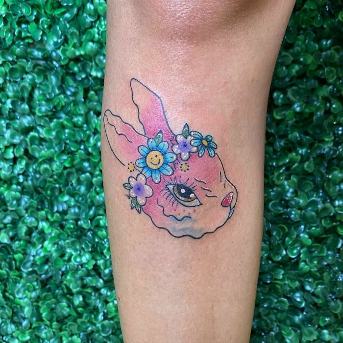 Ethereal watercolor tattoo of a pink rabbit with floral crown on the forearm.