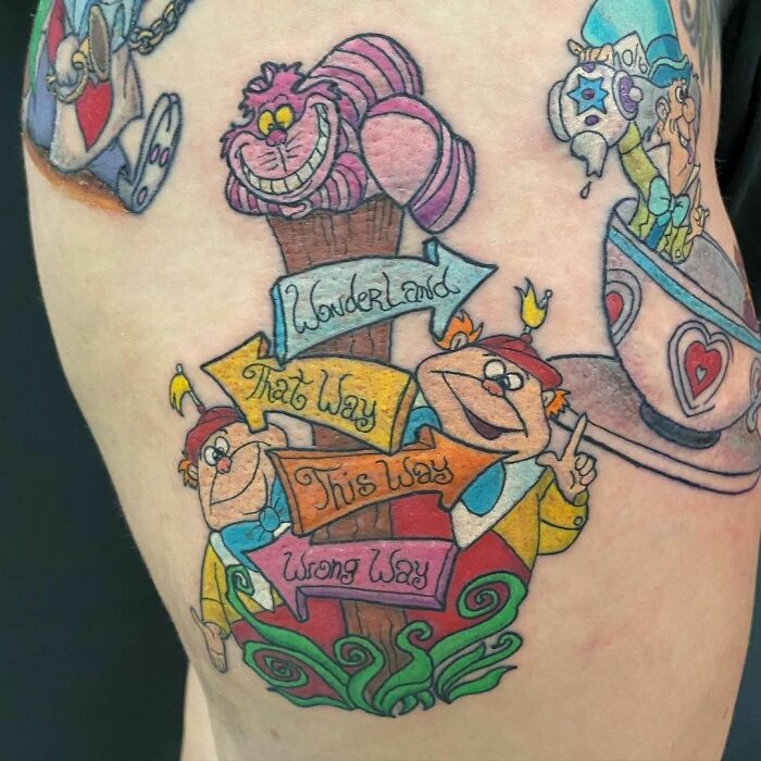 Colorful cartoon tattoo featuring Wonderland characters and directional signs.